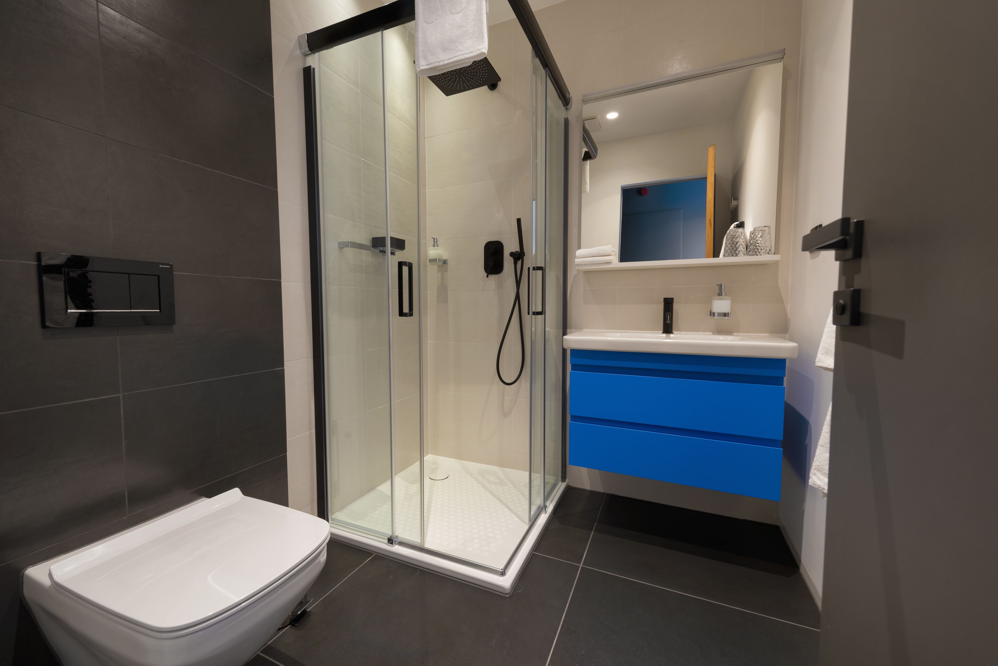 A modern bathroom with a glass-enclosed shower, a white toilet, and a vanity with blue drawers.