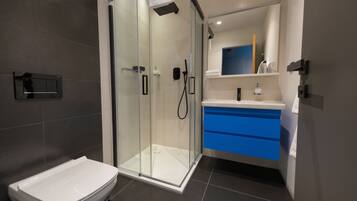 A modern bathroom with a glass-enclosed shower, a white toilet, and a vanity with blue drawers.