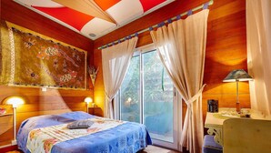 A bedroom with a large bed, a wooden ceiling, a window with curtains, a nightstand, and a lamp. - Pinpin d'Amour (Saint-Philippe)