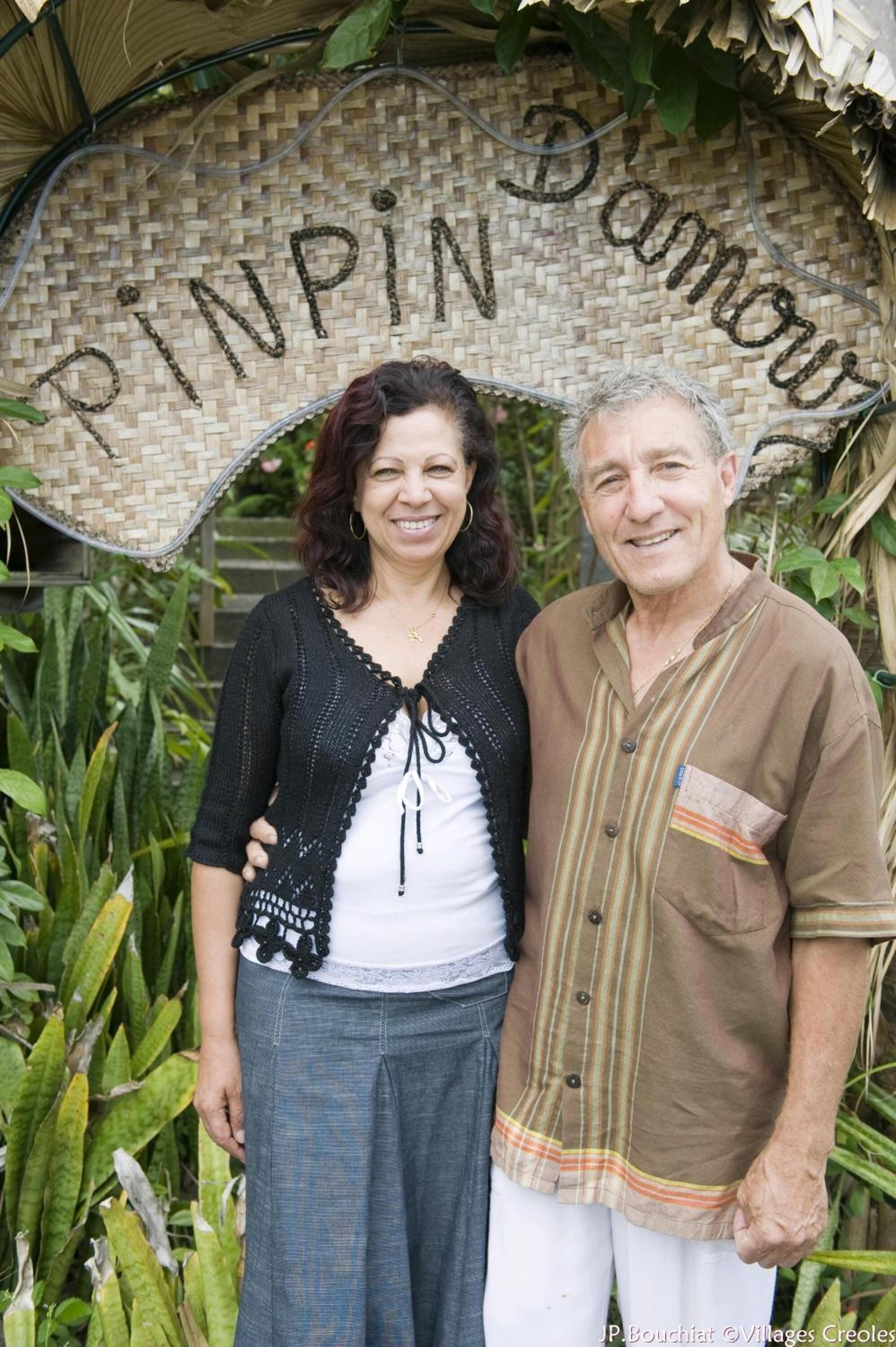 Two people standing in front of a woven sign with the text "PINPIN Damav".