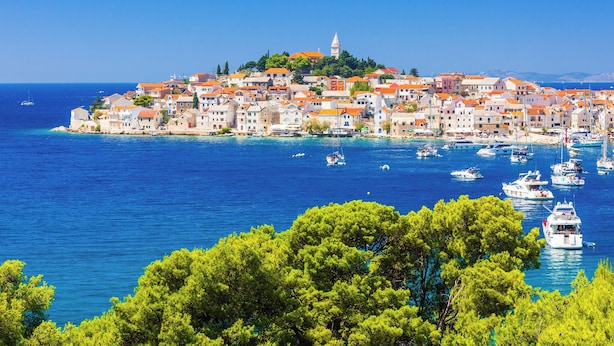 A coastal town with buildings on a hillside, boats in the water, and clear skies.