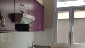 Una cocina con encimeras de granito, gabinetes morados, un lavamanos de acero inoxidable y una ventana con persianas.