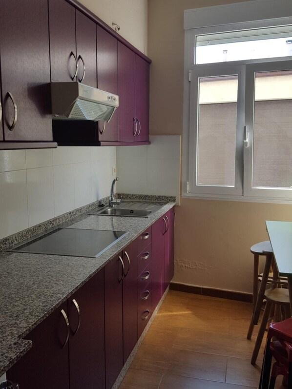 Eine Küche mit Granit Arbeitsplatten, violetten Schränken, einer Edelstahl-Spüle und einem Fenster mit Jalousien.