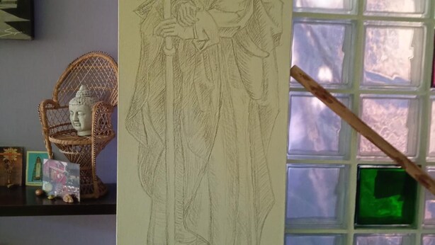 Un detallado dibujo a lápiz de una persona sosteniendo un báculo, expuesto en una pared cerca de un ventanal con vidrios esmeralda.