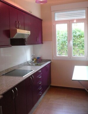 Una cocina con armarios morados, encimera de granito, una ventana con persianas y un lavabo.