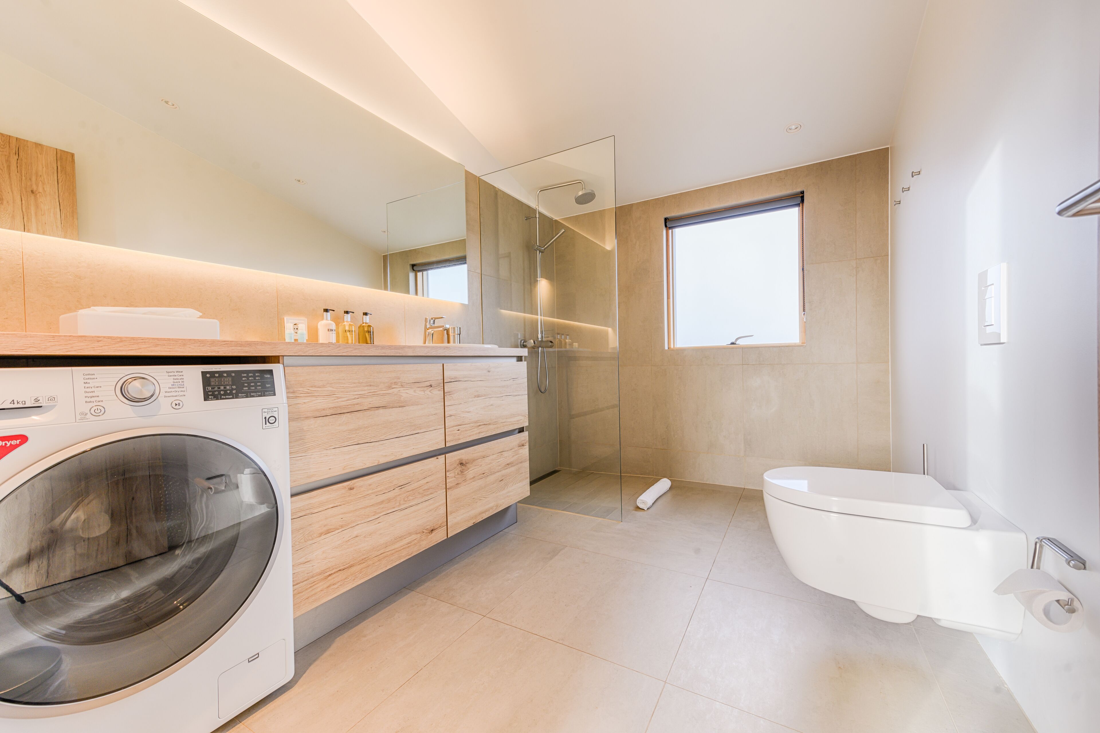 Un baño moderno con lavadora incorporada, cabina de ducha de vidrio y un inodoro.