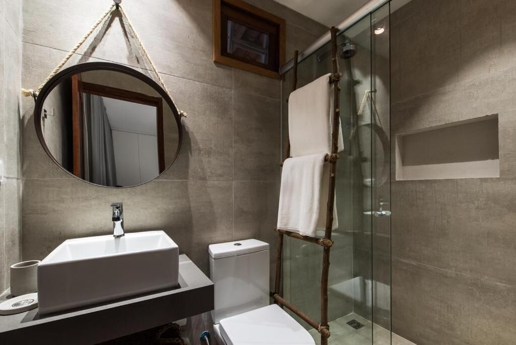 Une salle de bain moderne avec un grand miroir rond, un lavabo, des toilettes et une douche à parois de verre.