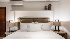 Een keurig opgemaakt slaapkamer met een bed, nachtlampjes, een airconditioning en een plank met decoratieve objecten.