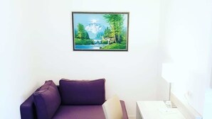 A small room with a purple sofa, a white desk, and a chair. There is a framed picture of a mountain landscape on the wall. - Hotel Restaurant Angelo (Saarbrücken)