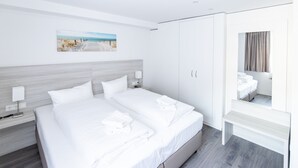A modern hotel room with a large bed, a bedside table, a nightstand, a wardrobe, and a bathroom mirror. - Hotel Restaurant Angelo (Saarbrücken)
