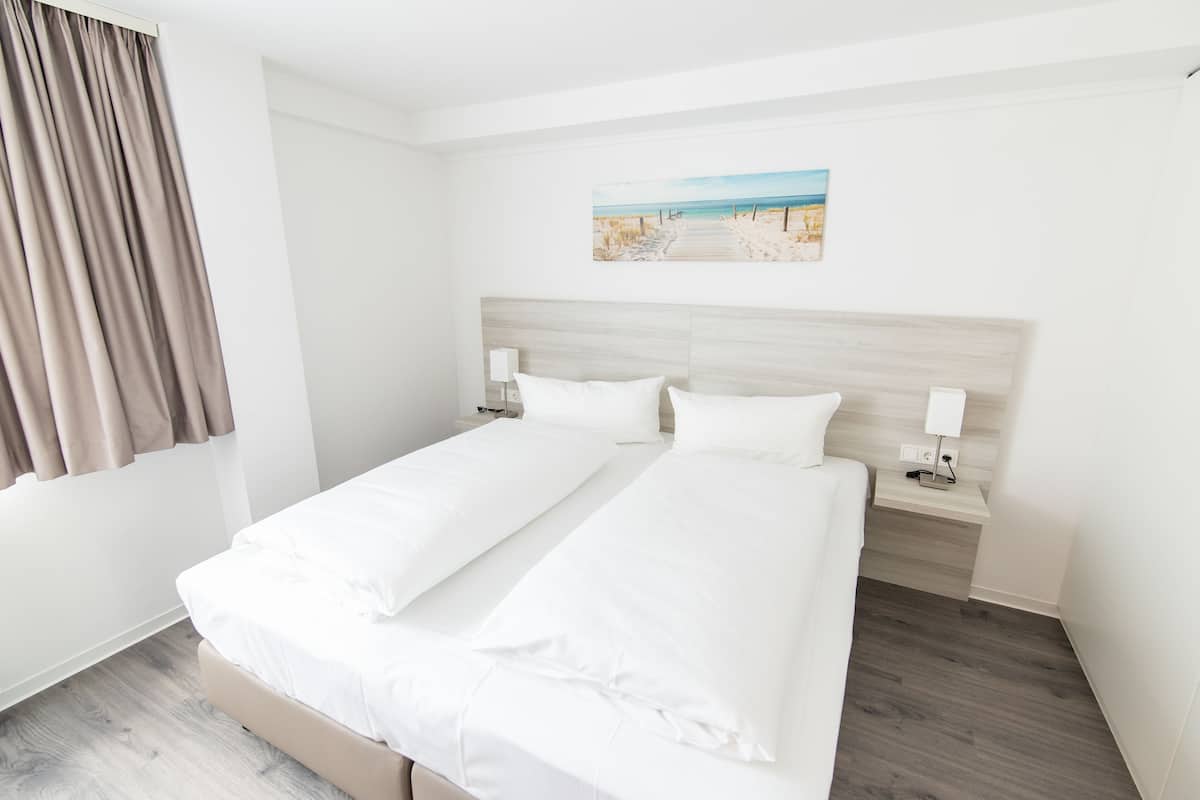 Un letto matrimoniale con lenzuola bianche, una testiera in legno, comodini con lampade e un quadro a tema spiaggia sulla parete.