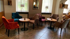 A room with a seating area featuring round tables and chairs, large windows with curtains, and a mirror on the wall. - Hotel Restaurant Angelo (Saarbrücken)