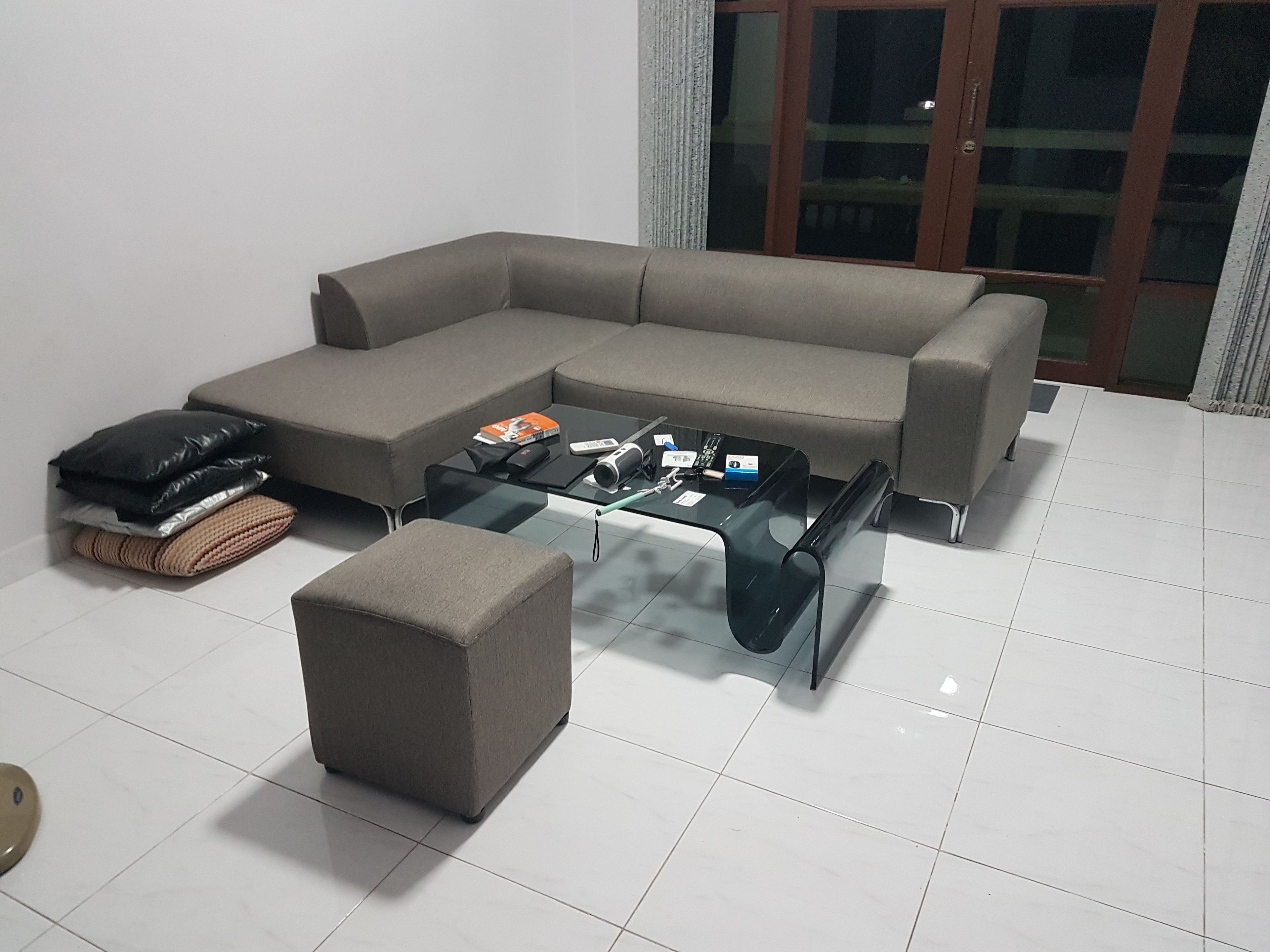Una sala de estar con un sofá modular, una mesa de centro de vidrio y un pequeño reposapiés.
