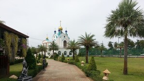 A pathway leading to a church with blue and gold domes, surrounded by palm trees and greenery.
