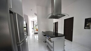 A modern kitchen with a stainless steel refrigerator, a central island with a black countertop, and a large range hood.