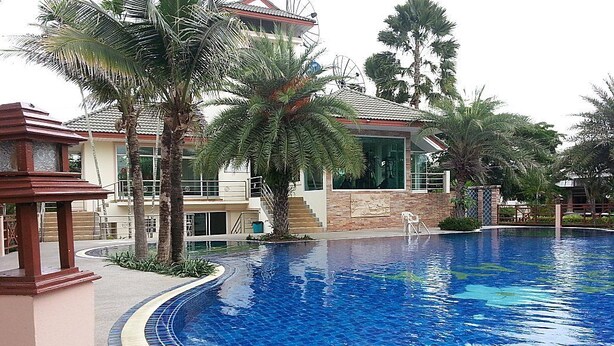 A swimming pool with a tiled edge, palm trees, and a building with a tiled roof and windows.