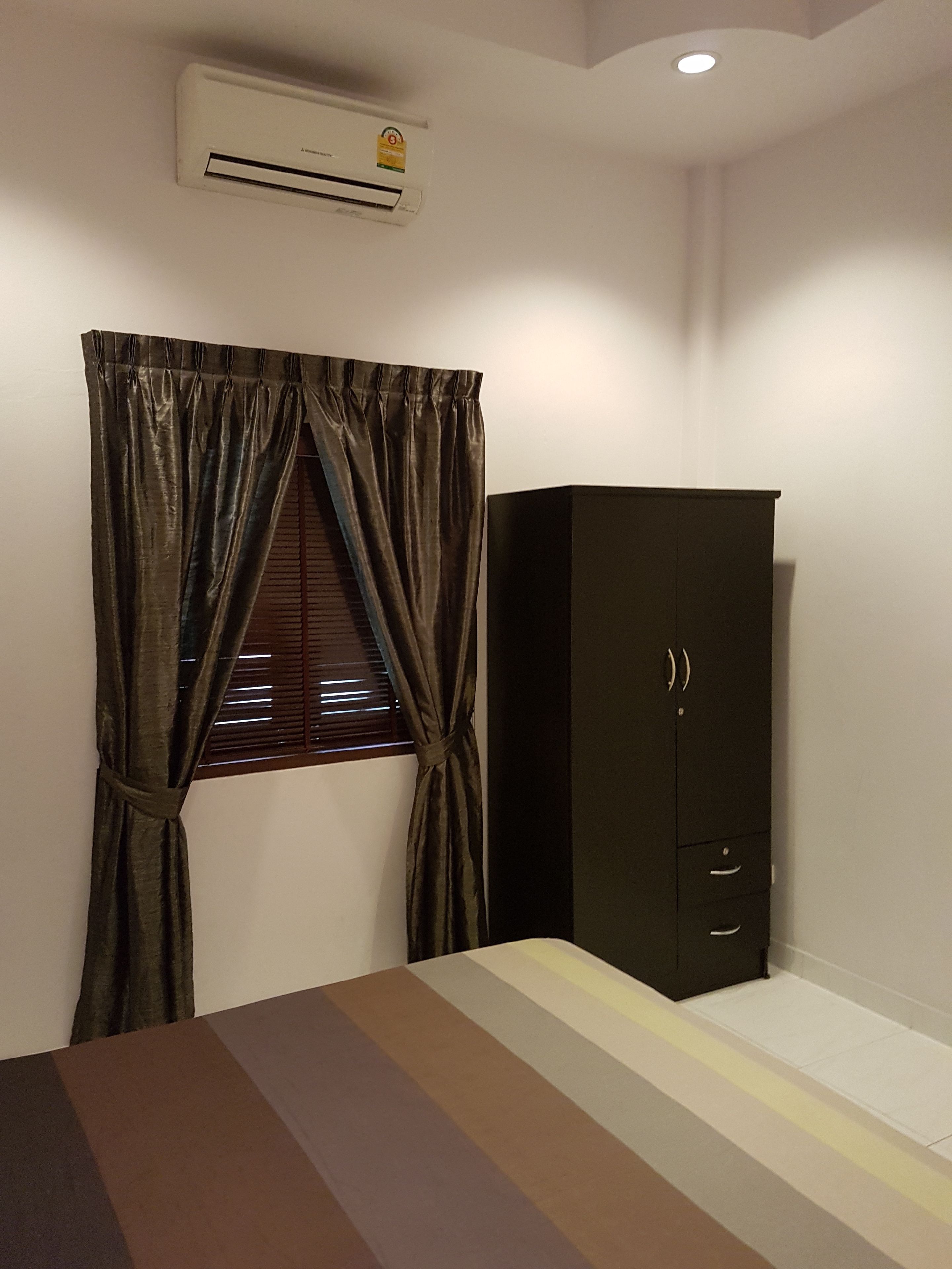 A bedroom with a bed, a wardrobe, a window with curtains, and an air conditioning unit.