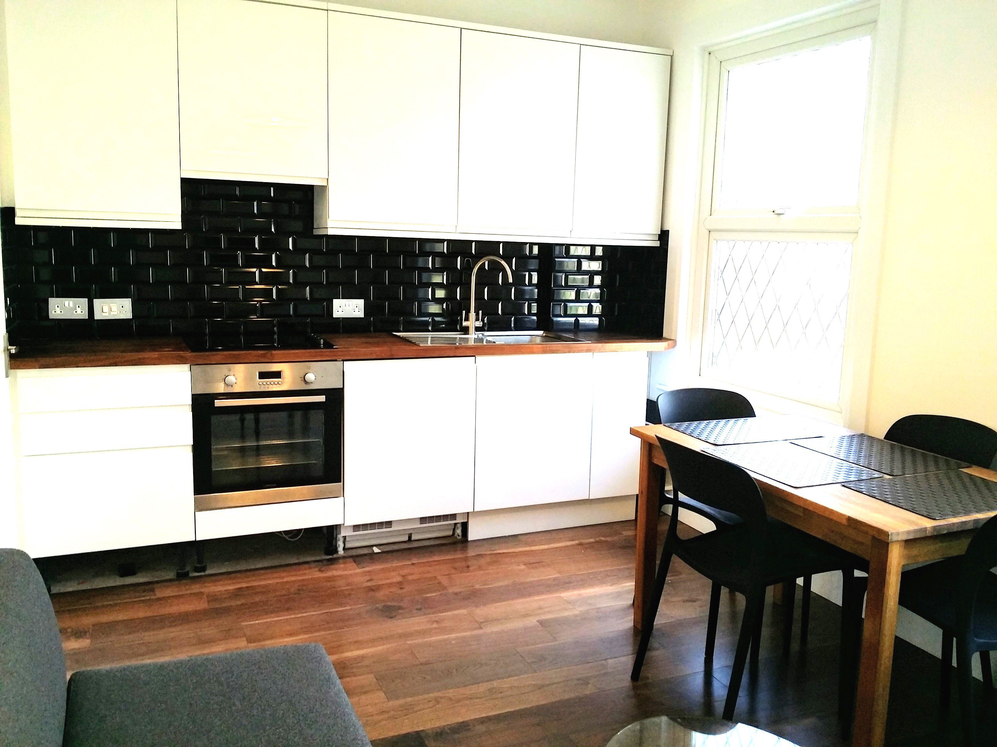 A modern kitchen with white cabinets, a black backsplash, and a wooden countertop.