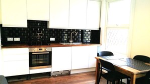 A modern kitchen with white cabinets, a black backsplash, and a wooden countertop. - Victorian Terraced Apartments (London)