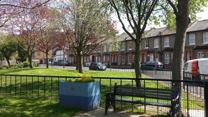 A residential street with houses, a bench, and a blue planter. - Victorian Terraced Apartments (London)