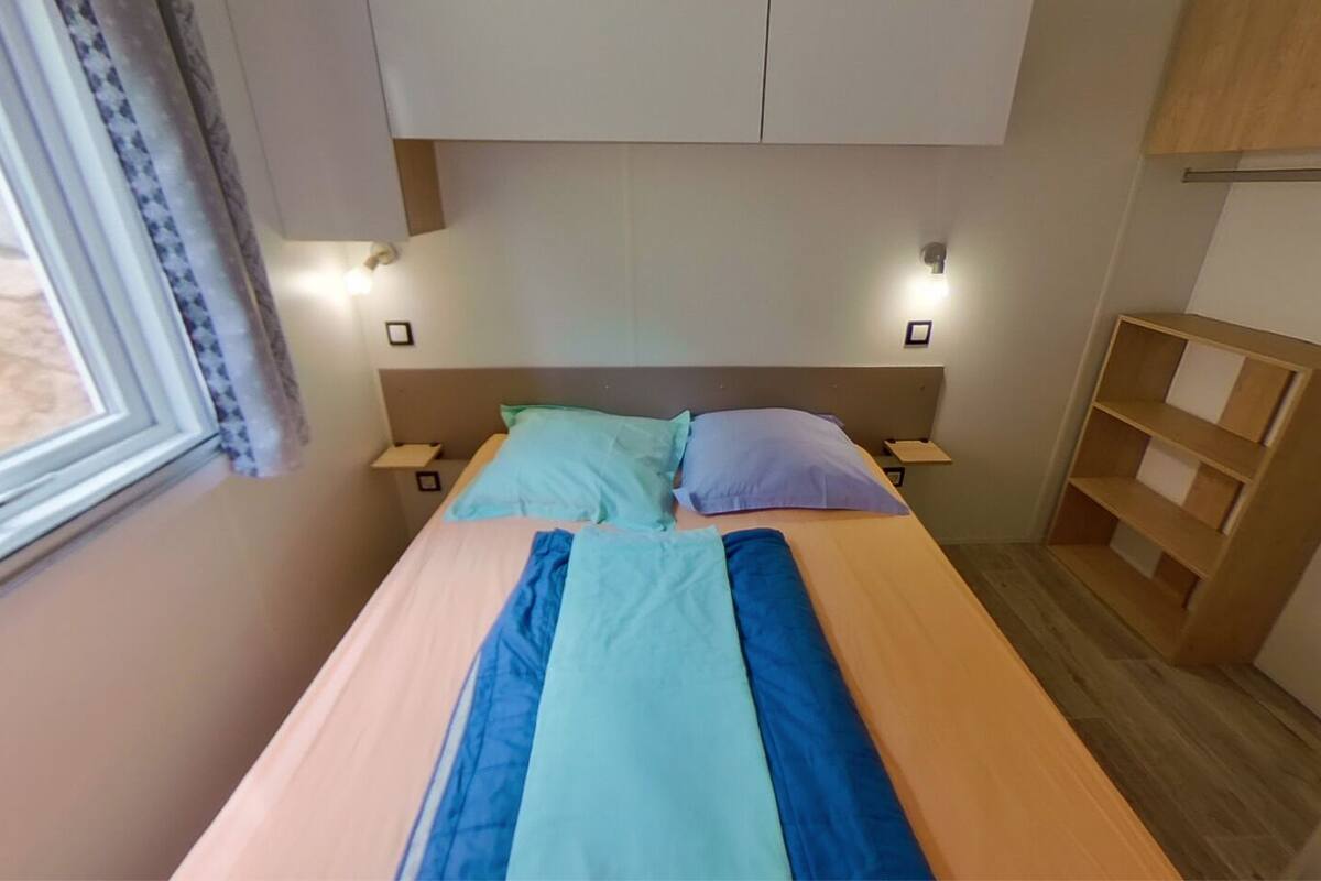 A single bed with two pillows, a bedside table, and a shelf unit.