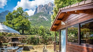 A rustic outdoor seating area with stone tables and chairs, a grill, and a view of mountains. - Funtana a l'ora (Ota)