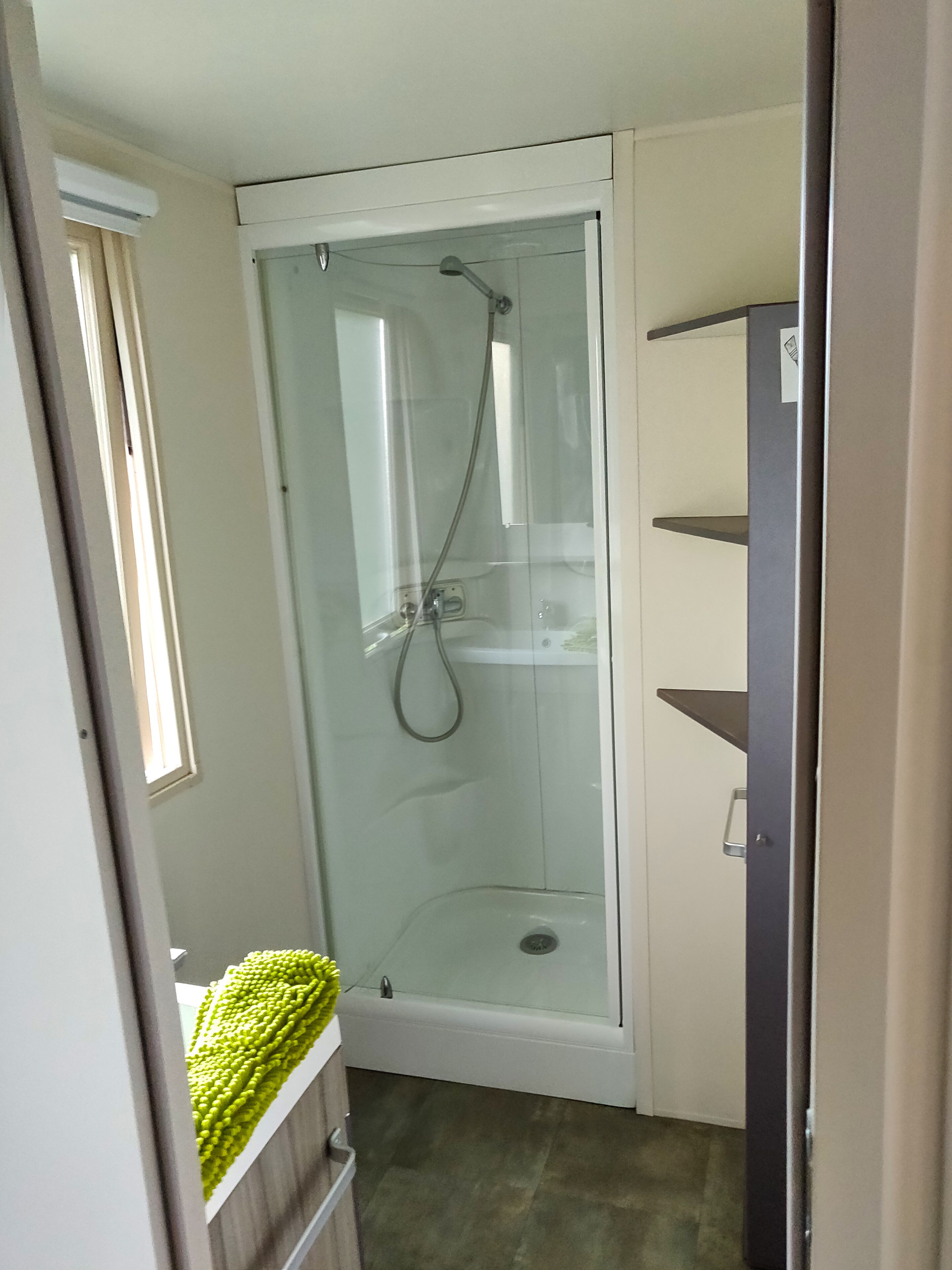 Een douchecabine met glazen wanden, een handdouche en een wandmengkraan.