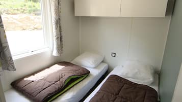 A small, compact room with two beds, a window with curtains, and a white cabinet above the beds.