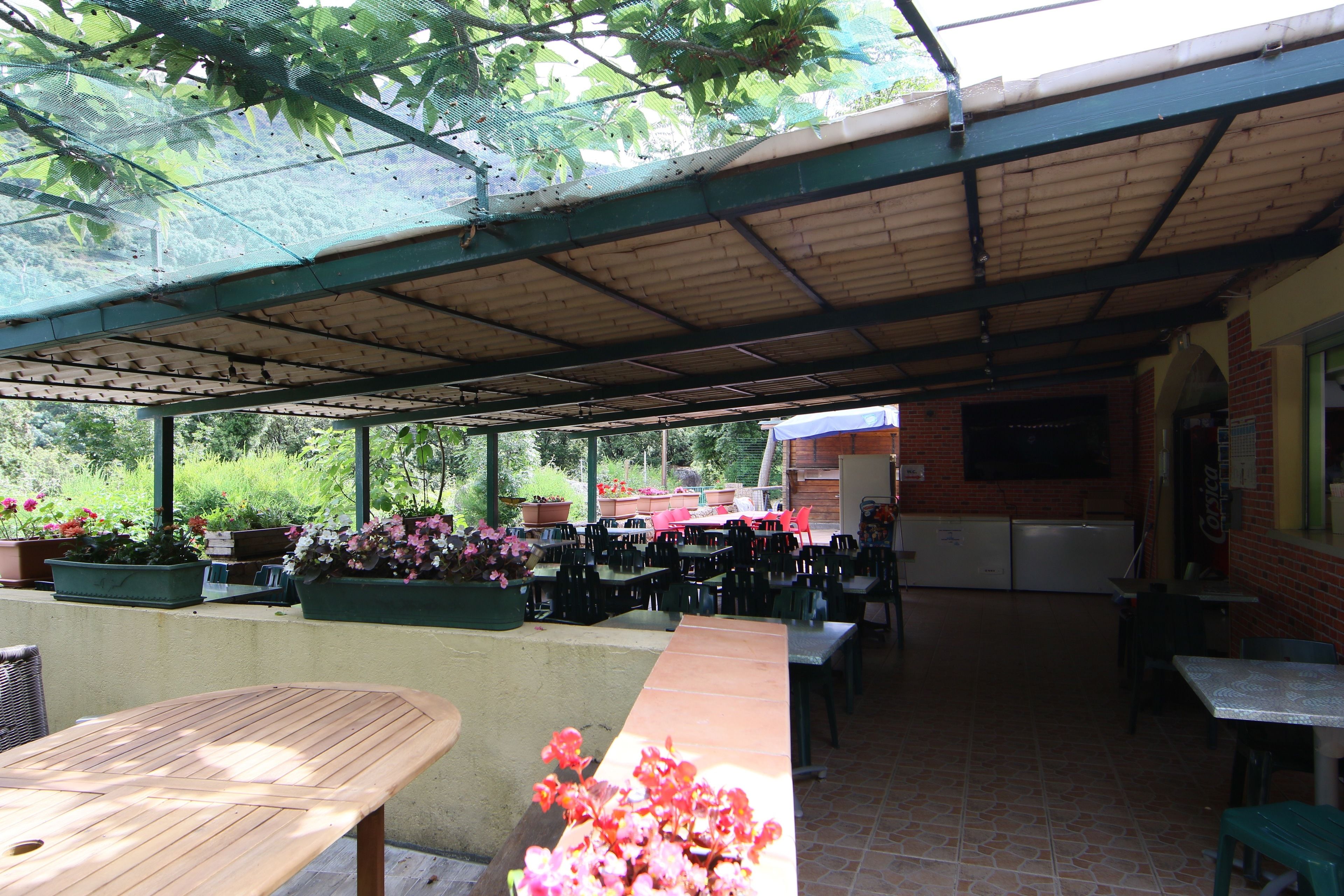Un espace extérieur aménagé en terrasse, avec des tables et des chaises, un coin salon abrité et des plantes en pot.