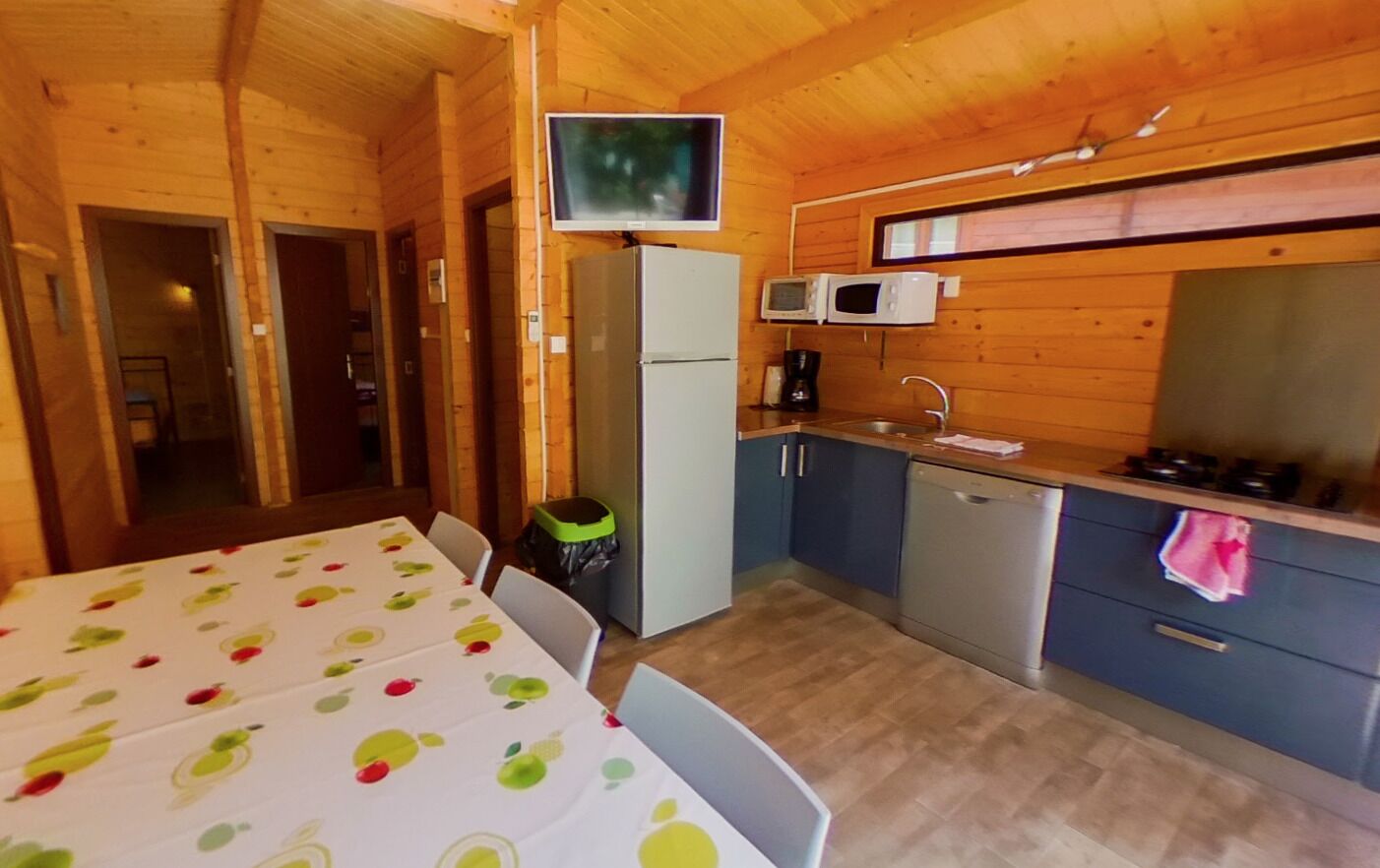 A compact kitchen with a refrigerator, microwave, sink, and a television mounted above the counter.