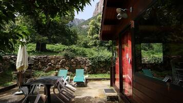 Una cabaña de madera con un patio, mobiliario exterior y vistas a montañas.