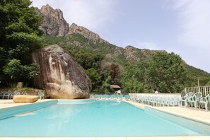 A swimming pool with lounge chairs, a large rock, and a mountain backdrop. - Funtana a l'ora (Ota)