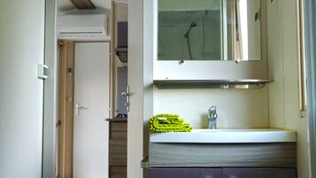 Een smalle gang die uitkomt bij een badkamer met een spiegel, wastafel en kastjes.