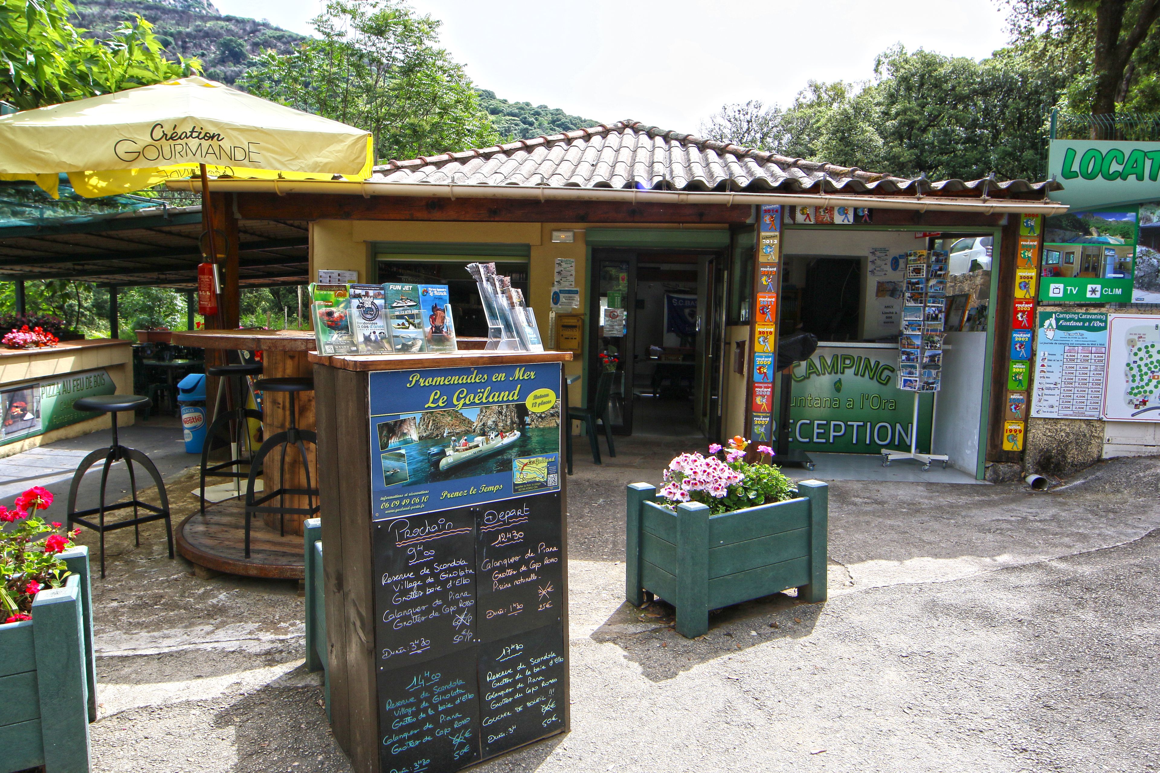 A small outdoor café with a yellow umbrella, a signboard with information, and a reception area.