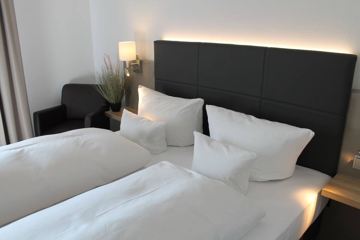 A hotel room with a large bed, two pillows, a bedside table with a lamp, and a chair.