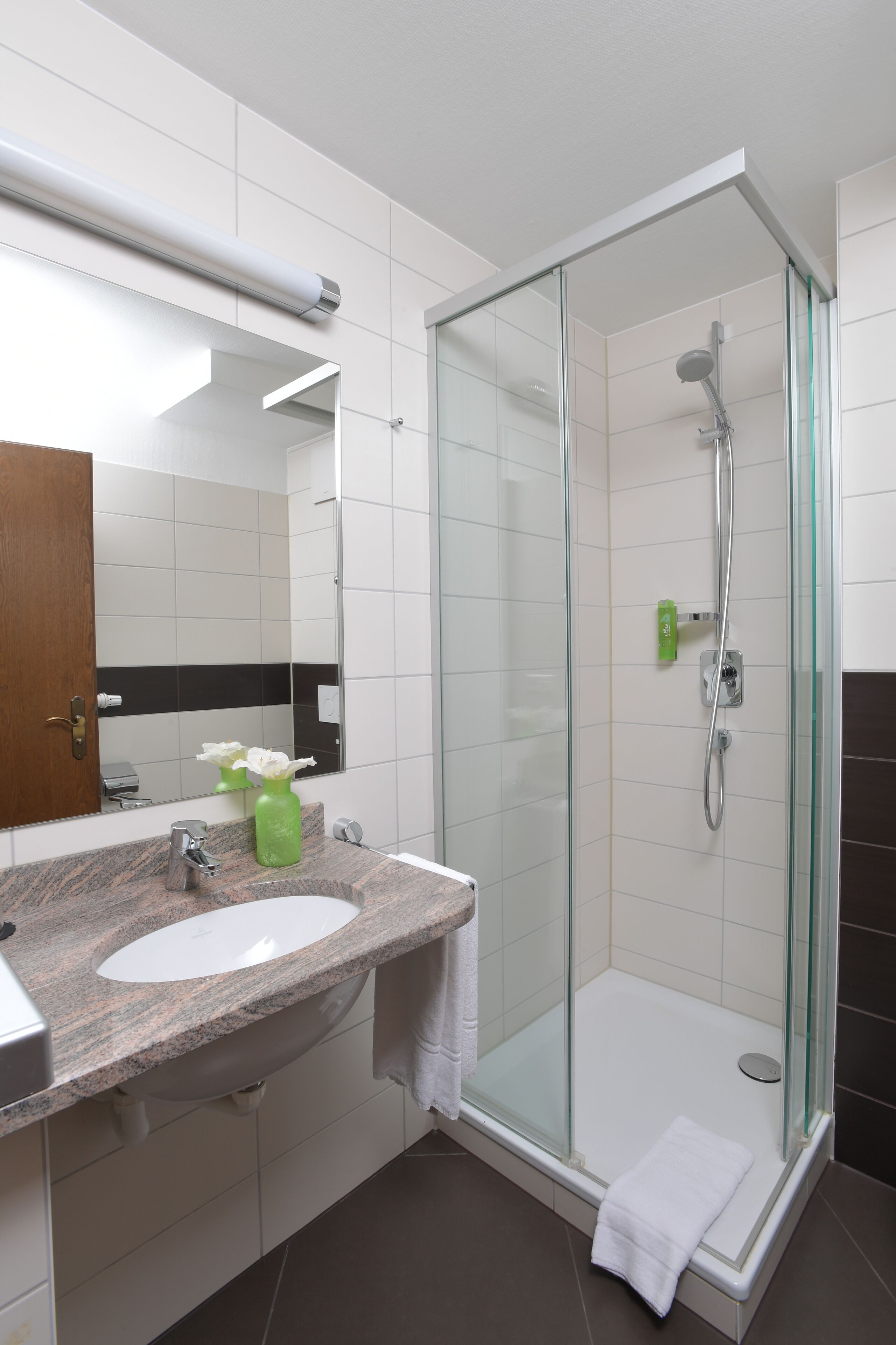 Un baño moderno con cabina de ducha de vidrio, lavamanos con encimera de granito y espejo sobre el lavamanos.