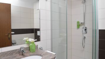 Un baño moderno con cabina de ducha de vidrio, lavamanos con encimera de granito y espejo sobre el lavamanos.