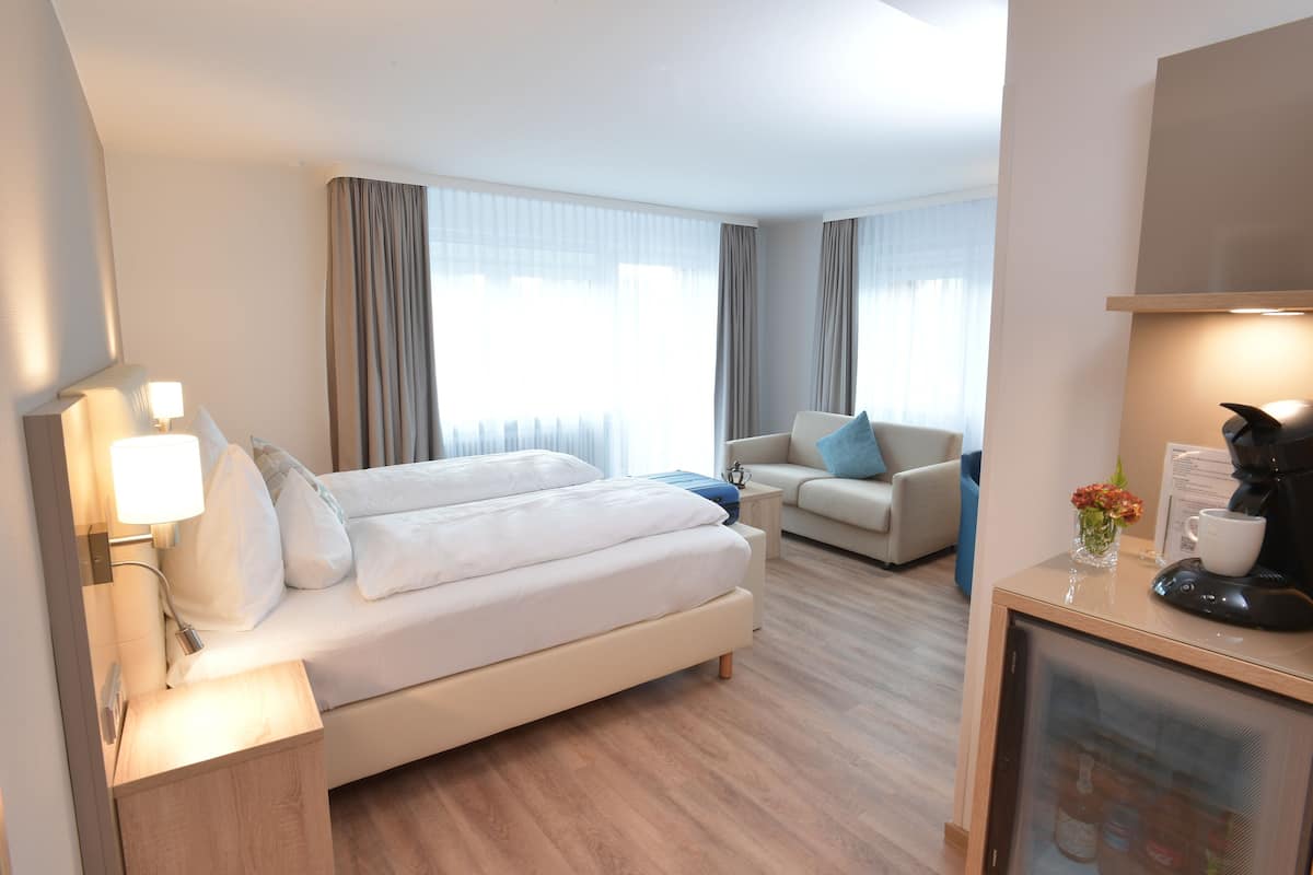 A hotel room with a bed, a sofa, a coffee machine, and a TV.