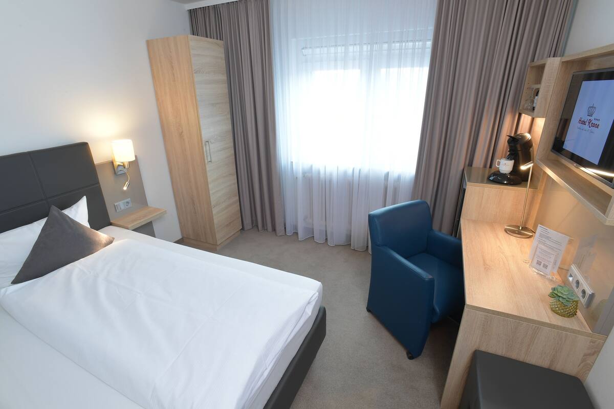 A hotel room with a bed, a desk with a computer, a chair, a wardrobe, and a window with curtains.