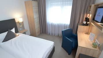 Ein Hotelzimmer mit Bett, Schreibtisch mit Computer, Stuhl, Kleiderschrank und Fenster mit Vorhängen.