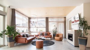 Un moderno vestíbulo de hotel con un conjunto de sofás, una mesa de centro, plantas en macetas y una chimenea.