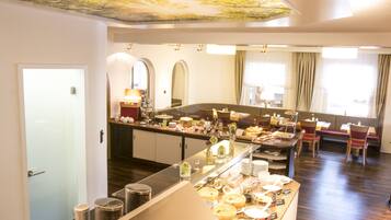 A breakfast buffet area with a variety of food options, a seating area with chairs and tables, and a ceiling with a nature-themed design.