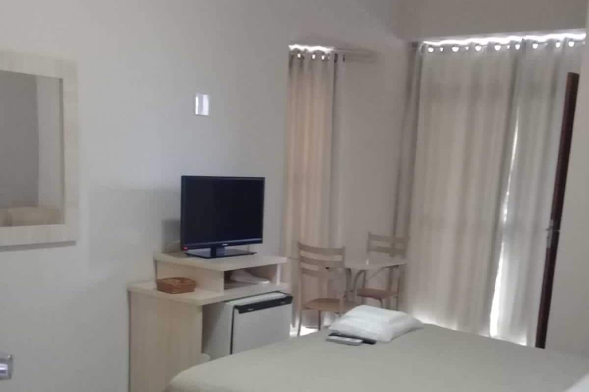 A hotel room with a bed, a television on a stand, a desk with a computer, and a chair.