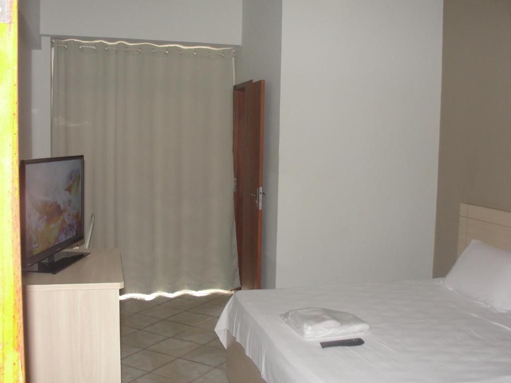 A hotel room with a bed, a television on a stand, a curtain, and a door.