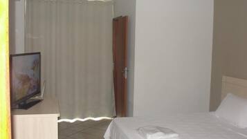 A hotel room with a bed, a television on a stand, a curtain, and a door.
