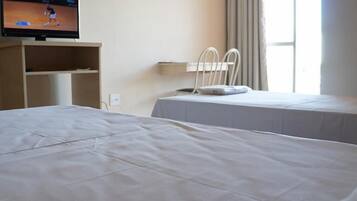Ein Hotelzimmer mit einem großen Bett, einem an der Wand befestigten Fernseher, einem Nachttisch und einem Fenster mit Vorhängen.