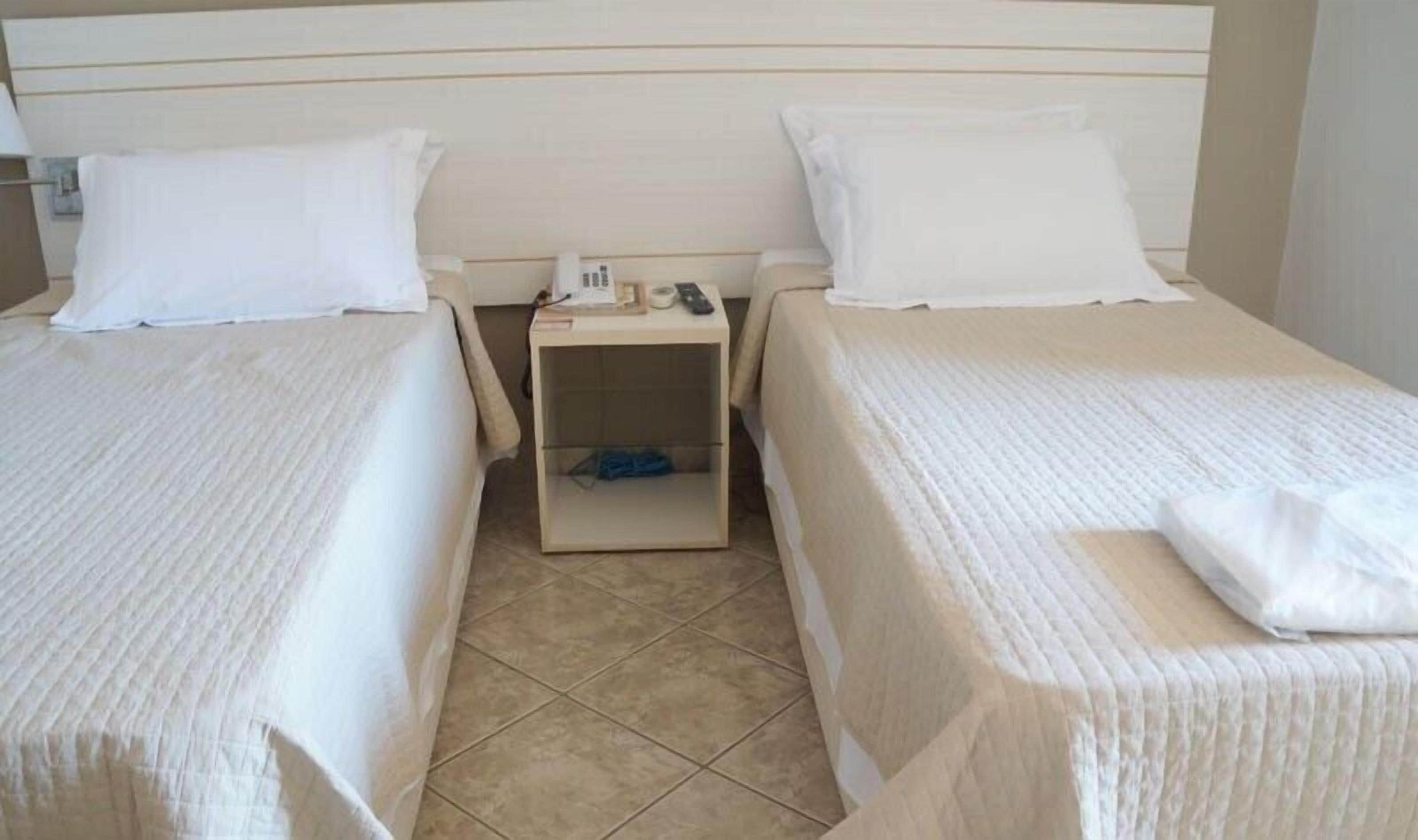 Een hotelkamer met twee eenpersoonsbedden, een nachtkastje met een lamp en een kleine opbergdoos.