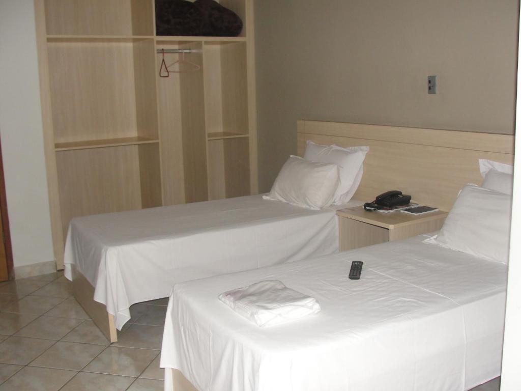Habitación de hotel con dos camas individuales, un armario de madera y una mesita de noche con teléfono y control remoto.