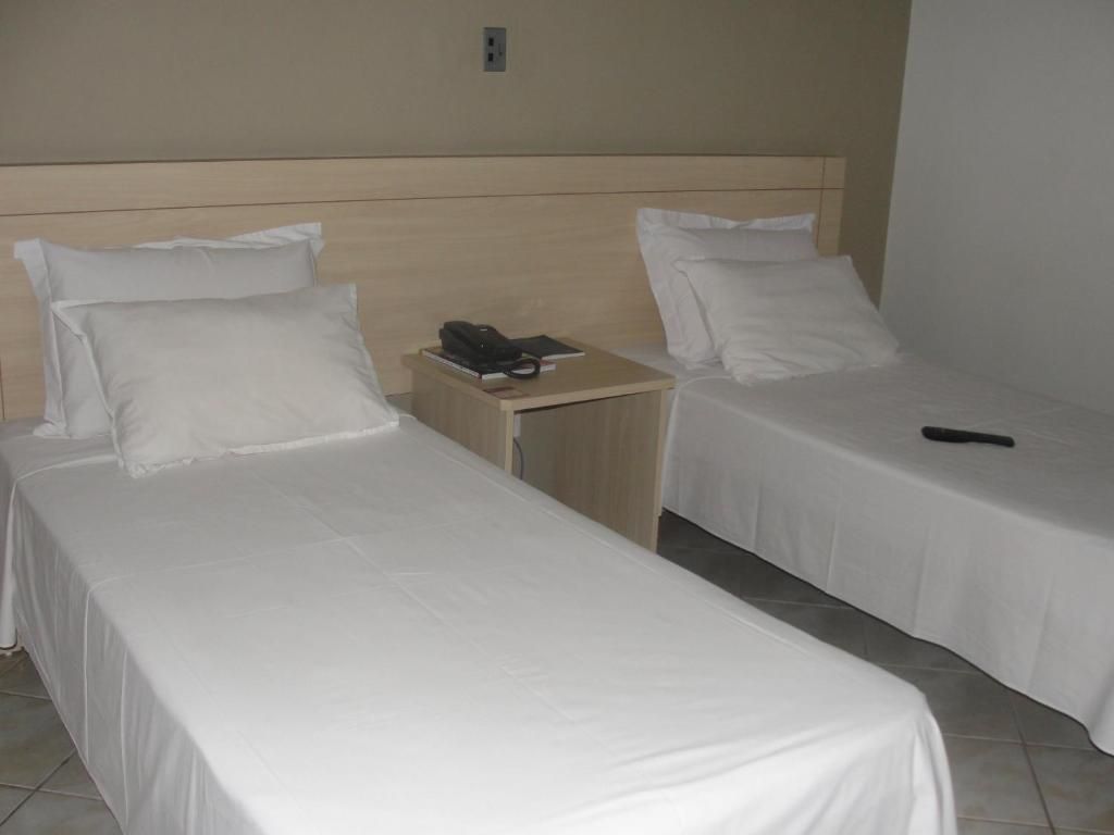 Una habitación de hotel con dos camas individuales, una mesita de noche de madera y una pared lisa.