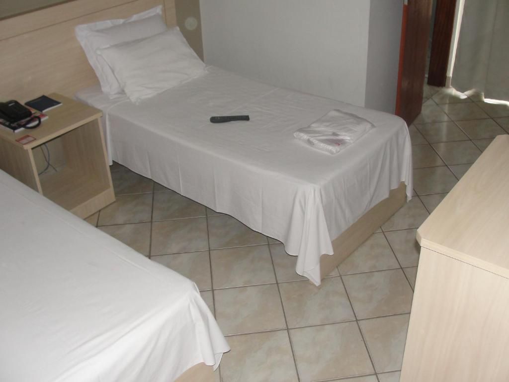 A single bed with a white bedspread, a bedside table with a book and a remote control, and a wooden nightstand.
